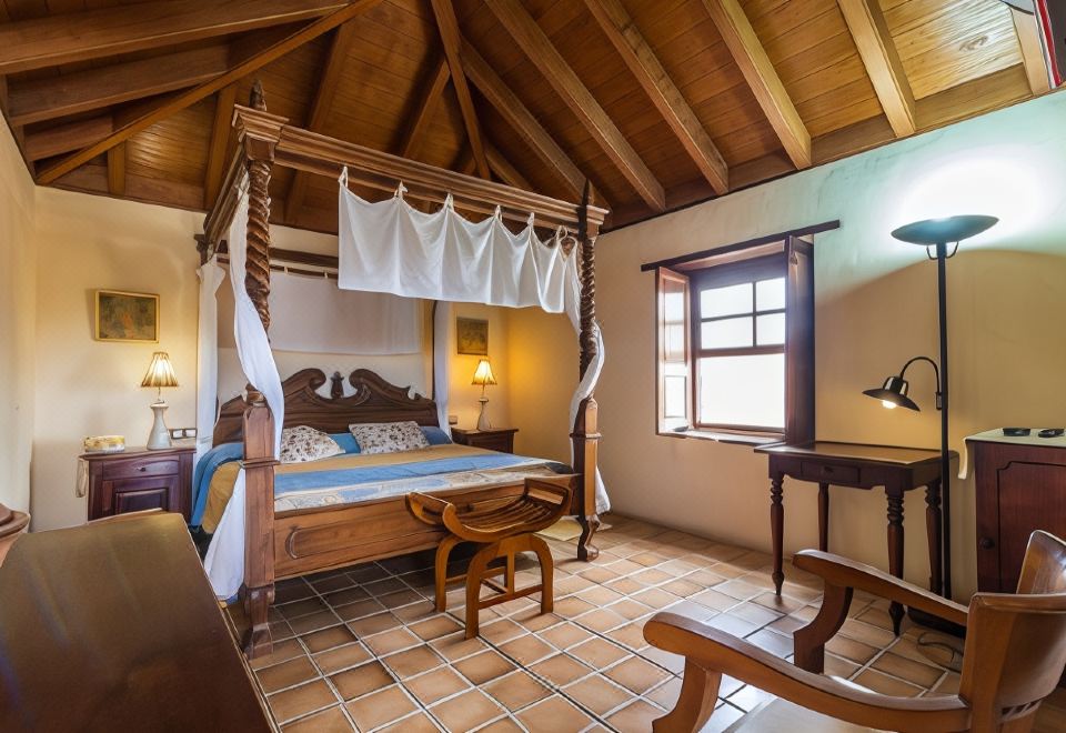 a bedroom with a wooden canopy bed , a chair , and a window overlooking the outdoors at Hotel Rural Restaurante Mahoh