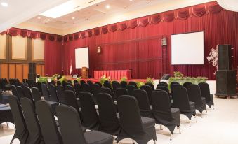 a large conference room with rows of black chairs arranged in a semicircle , and a podium in the center at Luminor Hotel Jember by WH