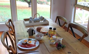 a wooden dining table with a variety of breakfast items , including eggs , bacon , toast , and coffee at Abby's Cottages