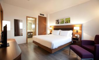 a large , neatly made bed is the centerpiece of a hotel room with wooden floors and white bedding at Hilton Garden Inn Malaga