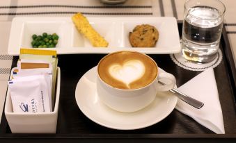 a cup of coffee with a heart design on it is placed next to a plate of cookies and a glass of water at Hotel Ciputra Cibubur Managed by Swiss-Belhotel International