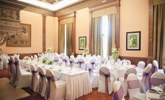 a large , elegant banquet hall with white tablecloths and purple napkins is set up for a formal event at Macdonald Elmers Court Hotel