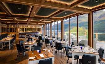 a large dining room with wooden tables and chairs , along with a view of the mountains outside the window at The Whispering Pine Lodge