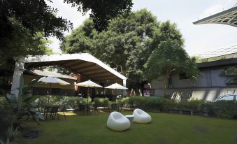 a modern outdoor seating area with a large tree in the background and several white lounge chairs arranged around it at Micasa Hotel
