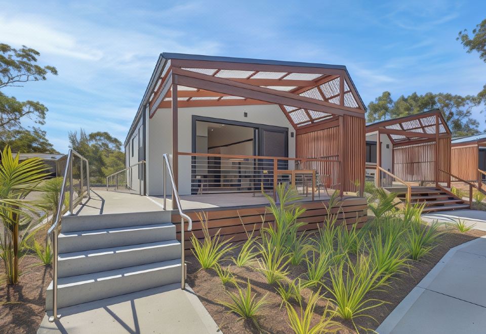 a modern , two - story house with a wooden deck and large windows , surrounded by lush greenery at Reflections Jimmys Beach - Holiday Park