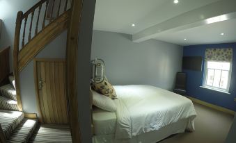 a large bed with white linens is situated in a room with wooden stairs and blue walls at The Feathers