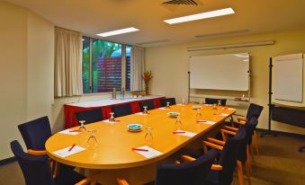 a conference room with a long wooden table , several chairs , and a projector screen in the background at Travelodge Resort Darwin