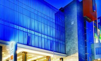 a modern building with blue glass walls and a gray metal structure , under a clear blue sky at Golden Flower by Kagum Hotels