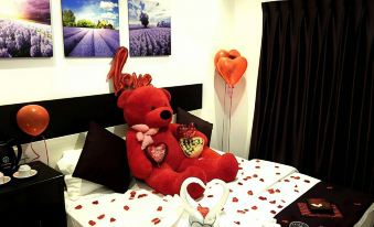 a red teddy bear is sitting on a bed with hearts and balloons , surrounded by pictures of lavender at Hotel Lavender Senawang