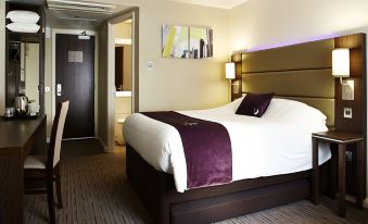 a large bed with a purple blanket and white pillows is in a room with a sink at Premier Inn Derby East