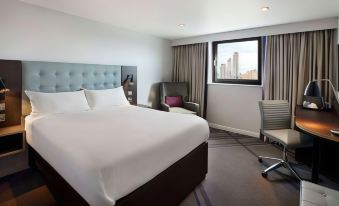 a hotel room with a large bed , white sheets , and a view of the city through a window at Premier Inn London Romford West