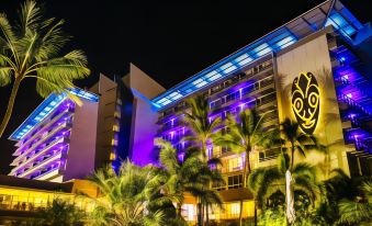 a large hotel building with purple lights illuminating its exterior , surrounded by palm trees at night at Chateau Royal Beach Resort & Spa, Noumea