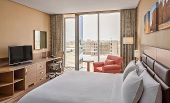 a hotel room with a large bed , a desk , a chair , and a window overlooking the city at Hilton Garden Inn Tabuk