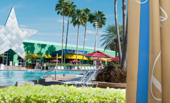 a hotel with a pool surrounded by palm trees , chairs , and umbrellas for guests to relax at Disney's All-Star Sports Resort