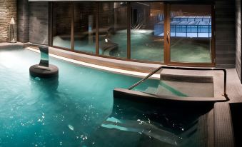 an indoor swimming pool with a hot tub , surrounded by glass walls and wooden flooring at Hotel Val de Neu G.L.