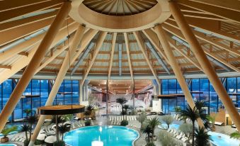 a large indoor swimming pool surrounded by lounge chairs and umbrellas , with a wooden ceiling at Courtyard Basel