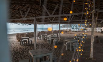 a beach restaurant with wooden tables and chairs , surrounded by palm trees and a view of the ocean at Cabana Retreat - Glamping