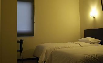 a bed with white sheets and a black chair in a room with yellow walls at Alpha Inn