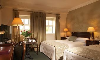 a hotel room with two beds , a window , and a table with flowers on it at Castle Hotel Macroom