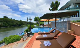 a pool area with several lounge chairs and umbrellas , overlooking a body of water and a bridge at Princess River Kwai Hotel