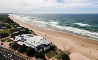 a beach scene with a building and people walking on the sand is shown from an aerial view at Coolum Caprice