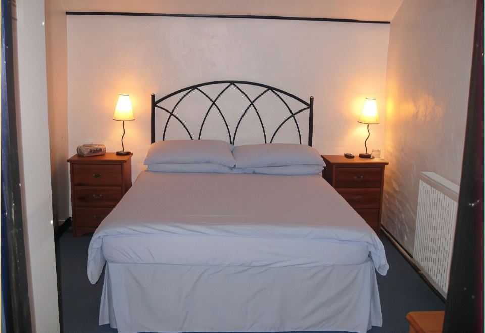 a bed with a black headboard and white sheets is situated between two lamps on either side at The Woodlands