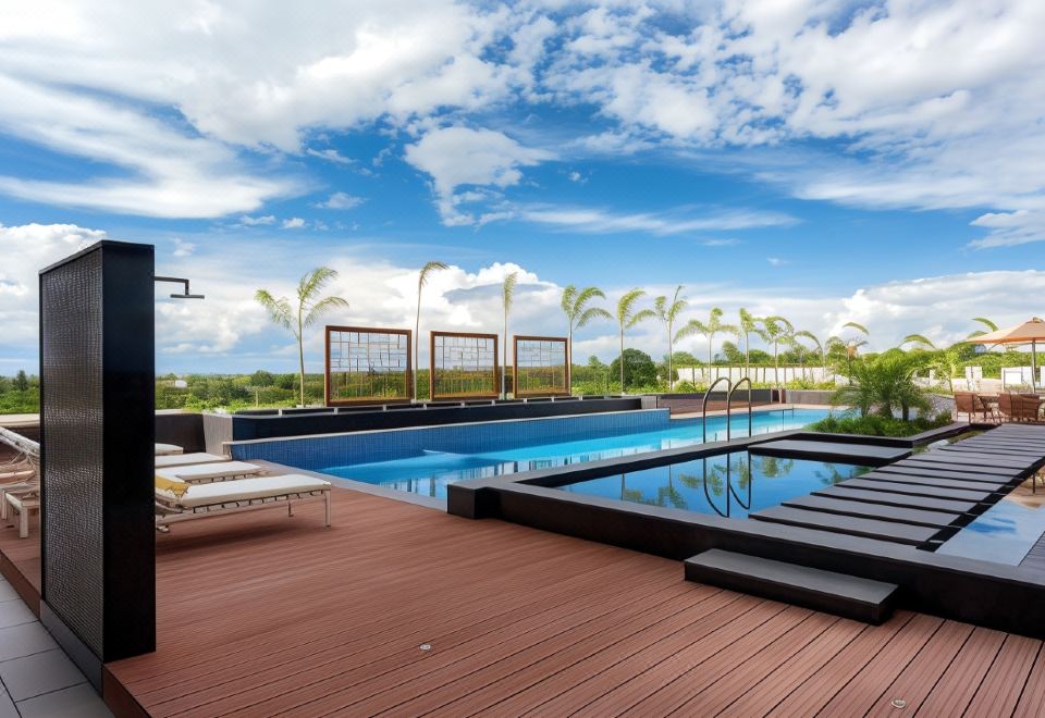 a large swimming pool with a wooden deck and lounge chairs is surrounded by palm trees at Neelkanth Sarovar Premiere