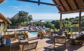 a luxurious outdoor area with a wooden deck , sun loungers , umbrellas , and an outdoor dining table surrounded by lush greenery at Bukela Game Lodge - Amakhala Game Reserve