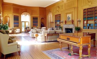 a large room with wooden floors and furniture , including a piano and several chairs , is adorned with paintings on the walls at Oheka Castle Hotel & Estate