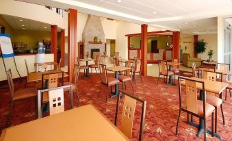 a large , empty dining room with multiple tables and chairs , a fireplace , and red carpeting at Comfort Inn & Suites Saratoga Springs