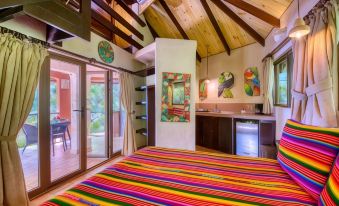 a cozy bedroom with a colorful striped bedspread , wooden beams , and an open door leading to a balcony at Ylang Ylang Beach Resort