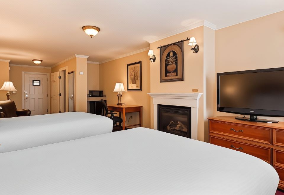a modern hotel room with white bedding , wooden furniture , and a fireplace , under a white ceiling with lamps at Best Western White House Inn