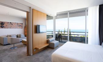 a modern hotel room with a large window offering an ocean view , featuring a bed , couch , and tv at Chateau Royal Beach Resort & Spa, Noumea