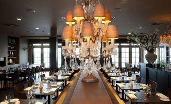 a long dining table with multiple chandeliers hanging from the ceiling , creating an elegant atmosphere at Fletcher Hotel - Restaurant Nautisch Kwartier