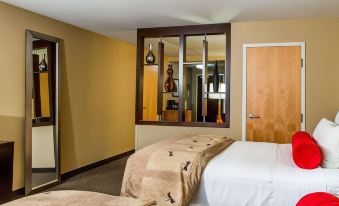 a modern hotel room with two beds , a mirror , and a red door , all decorated in neutral colors at Cambria Hotel Appleton