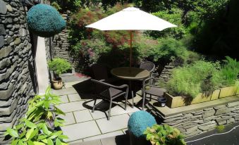 a patio with a table , chairs , and an umbrella is surrounded by potted plants and flowers at Woodlands