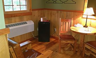 a cozy cabin interior with wooden walls , green paneling , and a black air conditioner , as well as two chairs and a table at Cranberry Inn