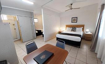 a hotel room with a bed , desk , and table is shown with a view of the bathroom through a window at Tropic Coast Motel