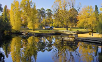 a serene landscape with a pond , trees , and a wooden bridge , reflecting the beauty of autumn at Abby's Cottages
