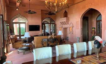 a spacious living room with pink walls , large windows , and multiple dining tables set for guests at Jodha Bai Retreat