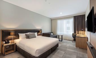a modern hotel room with a large bed , white bedding , and a brown leather ottoman at Ingot Hotel Perth, Ascend Hotel Collection