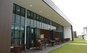 a modern building with large glass windows , outdoor seating area , and green grass under a cloudy sky at Lakeview Terrace Resort Pengerang