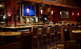 a bar area with several chairs and a television mounted on the wall , creating a comfortable atmosphere for patrons at DoubleTree by Hilton Hotel Cincinnati Airport