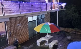 a patio with a colorful umbrella and a table , surrounded by a swimming pool and lit up lights at Hidden Inn