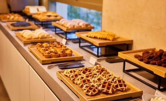 a variety of pastries and desserts are displayed on wooden trays in a room with large windows at Lotte City Hotel Ulsan