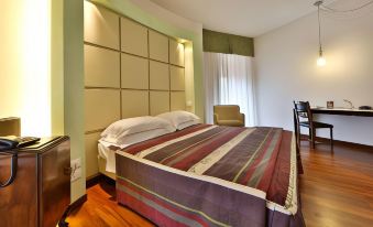 a large bed with a striped comforter is in a room with wooden floors and a window at Best Western Cesena Hotel