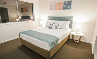 a bedroom with a large bed , two lamps , and framed pictures on the wall at Direct Collective - Breeze on Brightwater