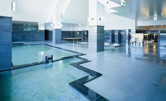 a large indoor swimming pool with blue water and white tiles , surrounded by a modern building at Furano la Terre