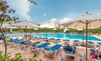 a large swimming pool with blue umbrellas and lounge chairs is surrounded by white buildings at Linda