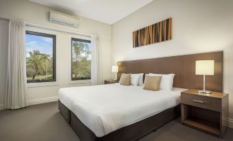 a large bed with white sheets and pillows is in a room with two windows at Quest Ipswich